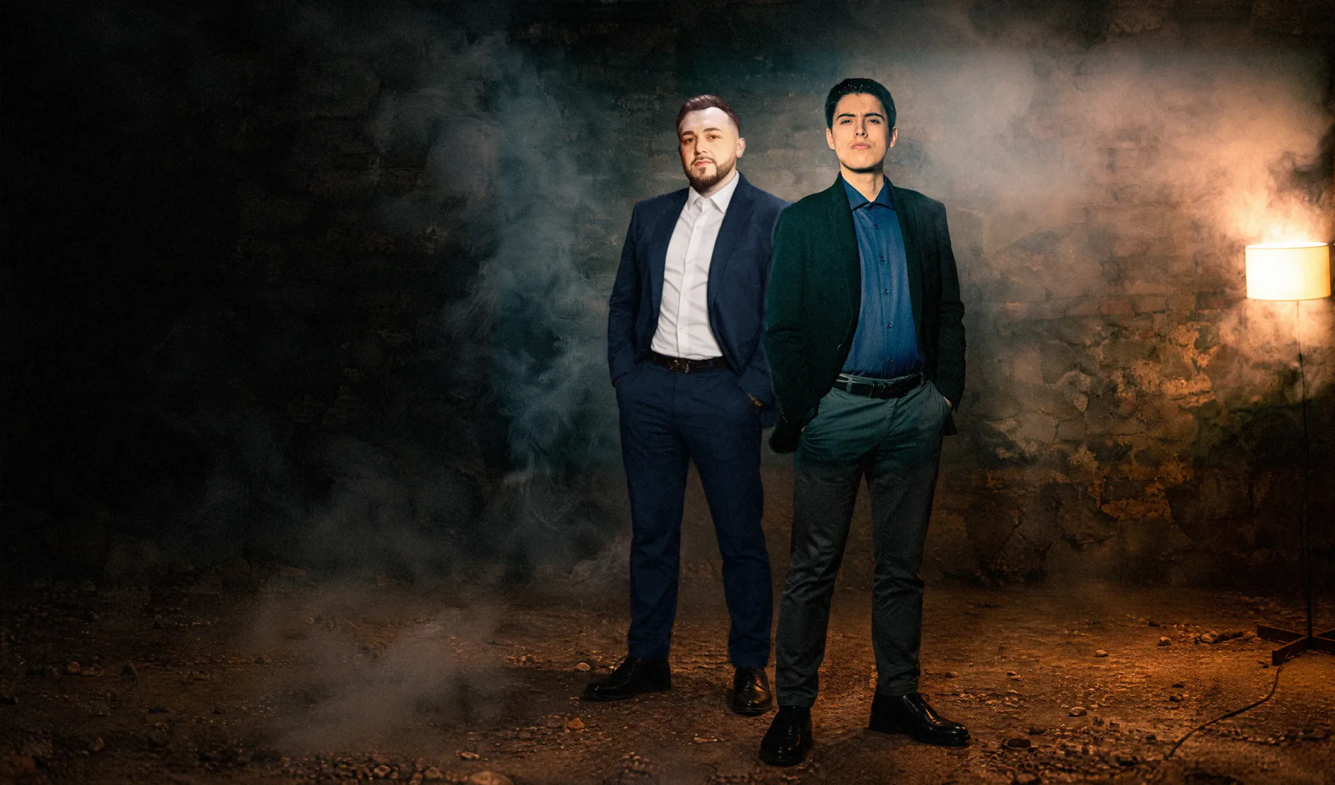Rado Sheytanoff and Chris Michael standing in a brick cellar, smoke and lamplight behind them