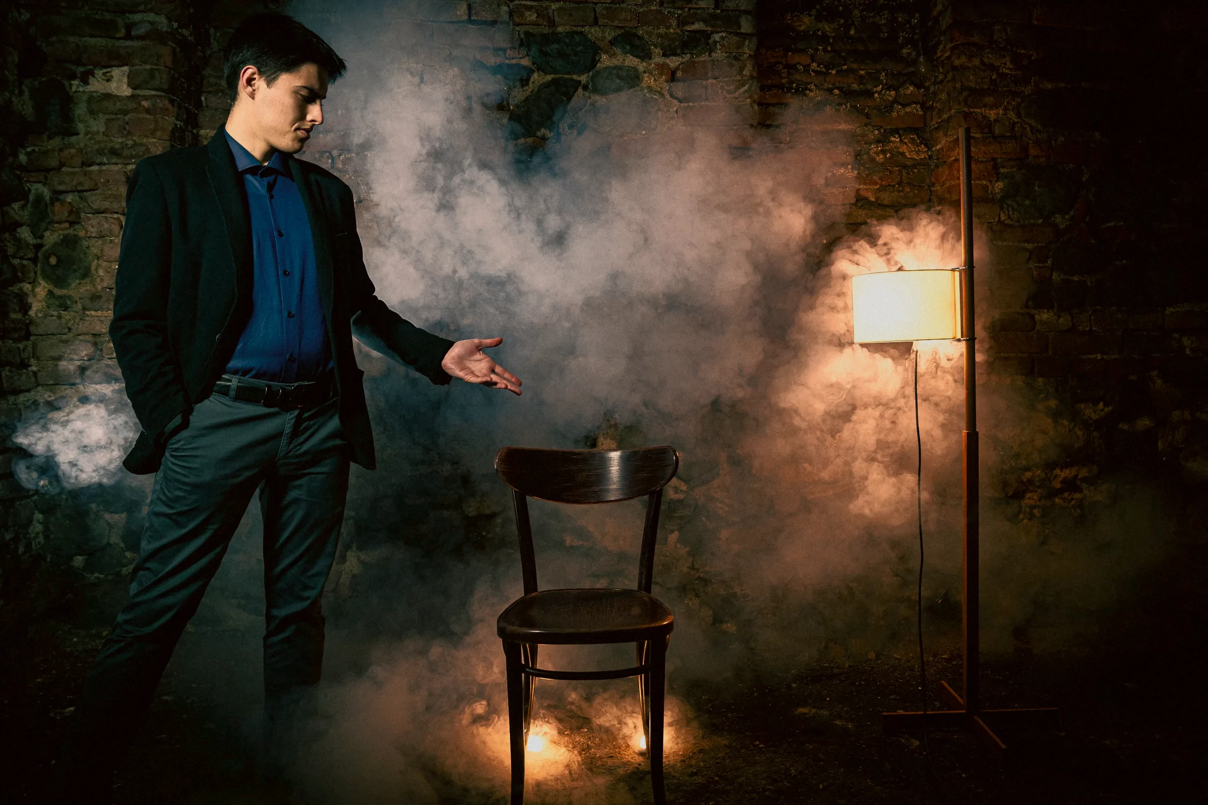 Rado offering the empty chair in the smoke of a brick cellar, a lamp and candles behind it