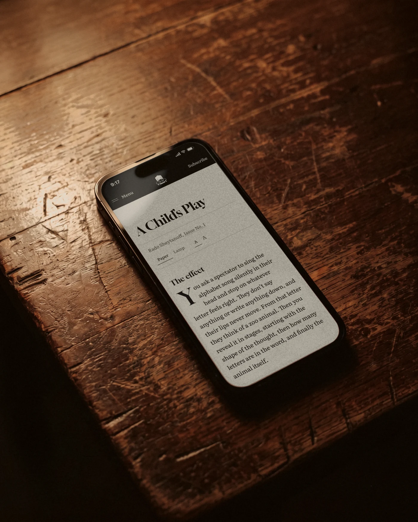 A Child’s Play open on a phone, lying on an old wooden table in lamplight